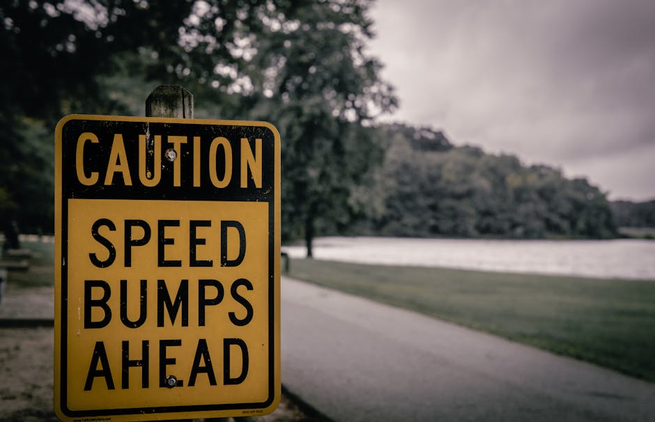 Yellow caution sign warning of speed bumps, placed in a park environment, overcast day.