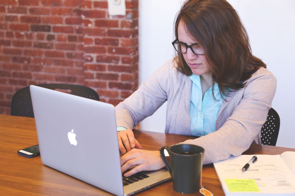 Young woman working on a laptop at a modern office desk with brick wall.