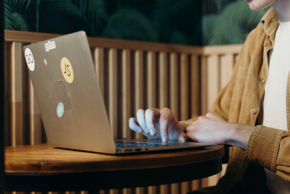 Person typing on a laptop in a cozy café, surrounded by greenery, enhancing focus and productivity.