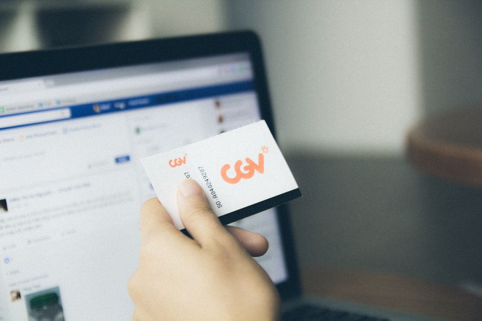 Close-up of a hand holding a card near an active laptop screen, indoors.