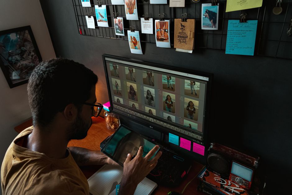 A young man edits photographs on a computer in a cozy home office setup.