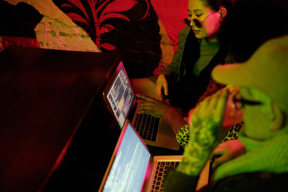 Young adults collaborating on coding projects in a trendy, dimly lit café setting.