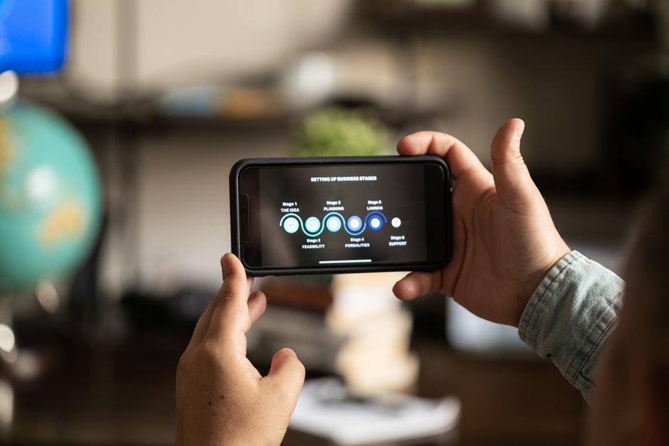 Hands holding a smartphone displaying business stages in a cozy indoor setting.