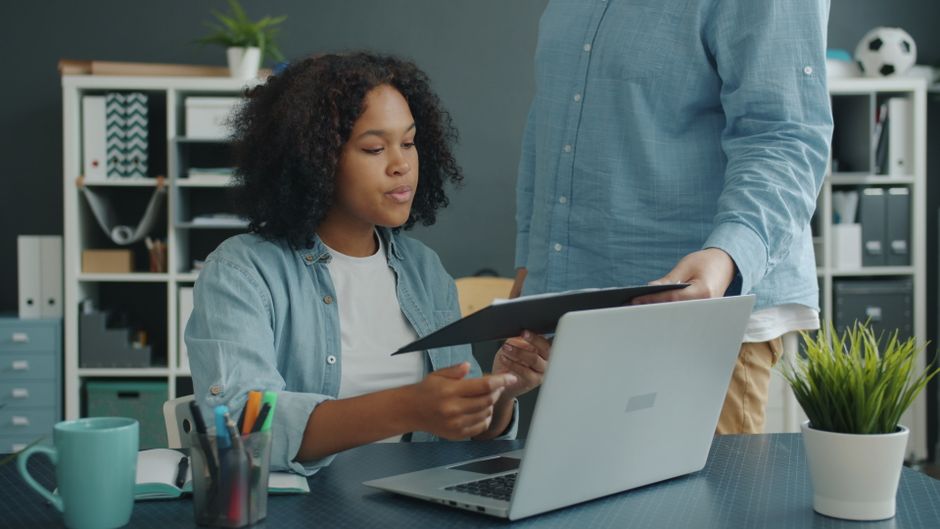 Two professionals collaborating in an office setting with a laptop and documents.