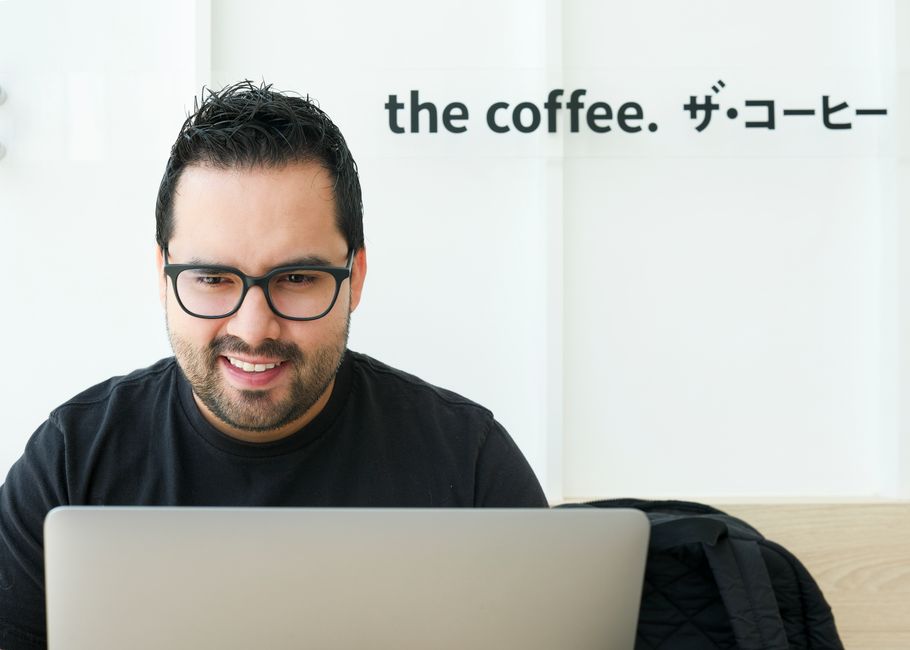 A smiling man using a laptop in a modern coffee shop setting indoors.