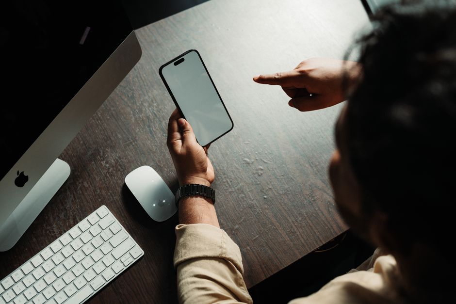 Person using a smartphone at a desk with a computer and peripherals.