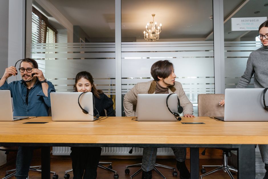 Business professionals working in an office with laptops and headsets, engaging in teamwork.