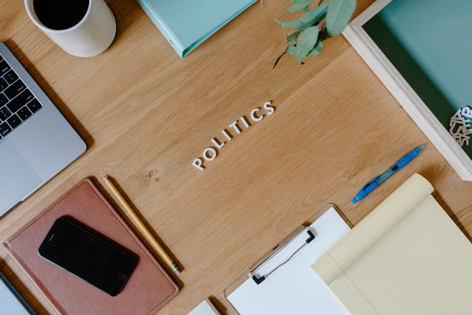 Overhead shot of a workspace with a politics theme, featuring a laptop, planner, and clipboard.